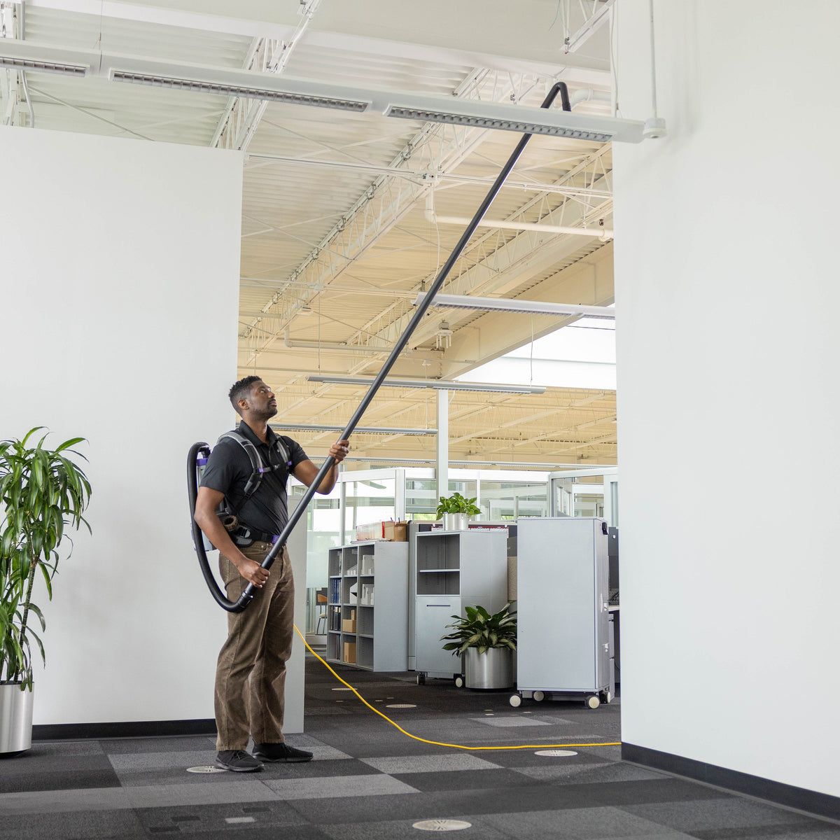 Dusting a high office light fixture from the floor with the GoHigh pipe tool